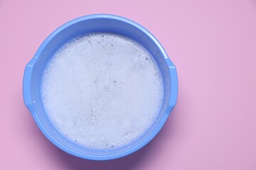 Blue plastic basin with water and foam on pink background, top view