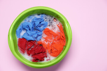 Plastic basin with clothes, water and foam on pink background, top view