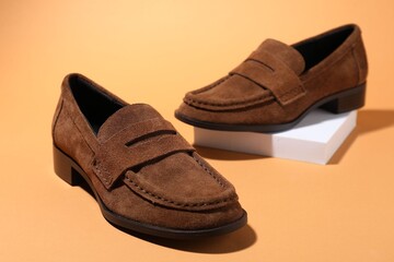 Pair of stylish brown shoes on pale orange background, closeup