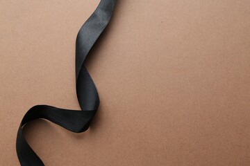 Beautiful black ribbon on light brown background, top view. Space for text