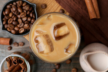 Tasty iced coffee with milk, cinnamon and beans on wooden table, flat lay
