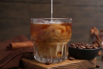 Pouring milk into iced coffee at wooden table, closeup