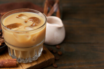 Tasty iced coffee with milk, cinnamon and beans on wooden table, closeup. Space for text