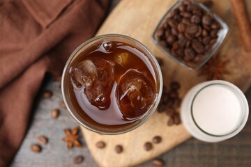 Tasty iced coffee in glass, milk and beans on wooden table, flat lay