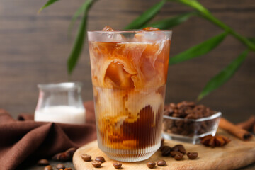 Tasty iced coffee in glass, milk and beans on wooden table, closeup