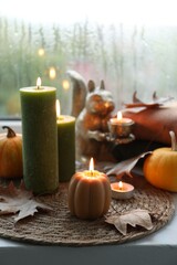 Burning candles and dry leaves on windowsill on rainy day. Autumn atmosphere