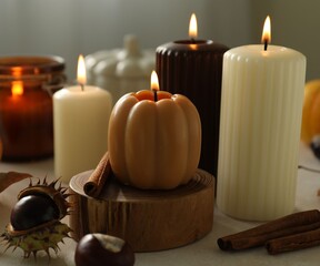 Different burning candles and autumn decor on white table indoors, closeup