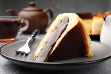 Piece of delicious Basque cheesecake with chocolate sauce and tea on grey table, closeup