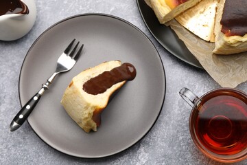 Delicious Basque cheesecake with chocolate sauce, tea and fork on grey table, flat lay