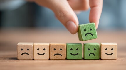 A hand lifts a green block with a sad face among others on a wooden table showing mood change.