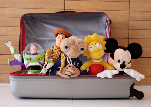Mickey Mouse, Buzz Lightyear, Woody, E.T. the Extra-Terrestrial and Lisa Simpson toys inside a luggage bag. Family vacation concept. Toys.