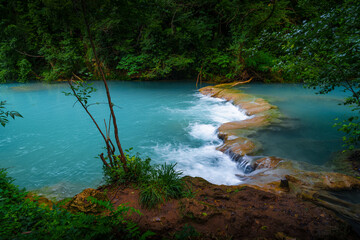 Obraz premium Turquoise river, rocky waterfall and greenery in summer forest