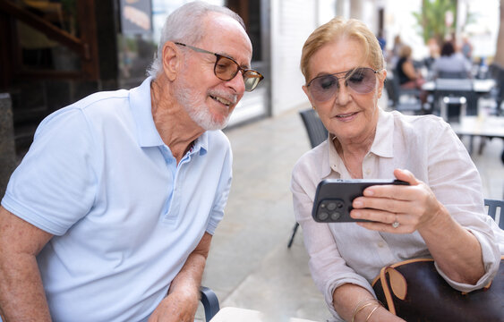 Portrait of a smiling senior mature couple using together smartphone sitting on a terrace outdoors. Technology concept.