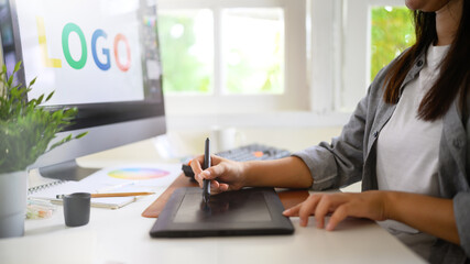 Graphic designer creating logo on digital tablet in bright modern workspace with computer and color palette