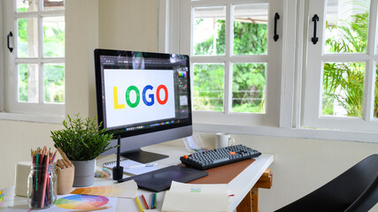 Creative woman designing logo sketches on notebook with color samples and tools in bright modern workspace