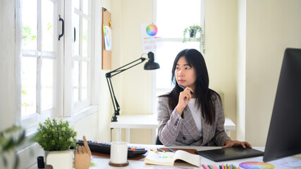 Creative woman thinking and planning new design ideas while working at desk with digital tablet in modern workspace