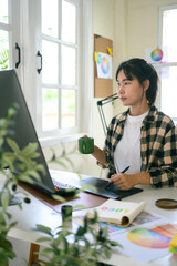 Graphic designer creating logo on digital tablet in bright modern workspace with computer and color...