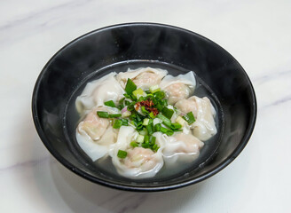 Chinese Wonton Dumpling Soup with Pork and Vegetable Filling Steamed Chinese Dim Sum in black bowl on marble background top view