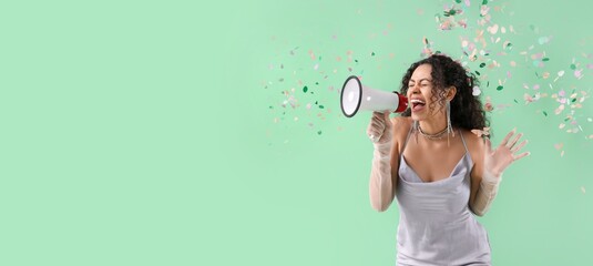 Fototapeta premium Young African-American woman with falling confetti shouting into megaphone on green background with space for text
