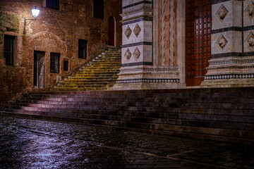 Naklejka premium Wet marble steps at Siena Cathedral entrance, ancient brick alley, night rain