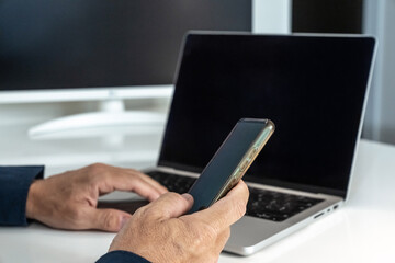 Professional simultaneously operating laptop and smartphone, highlighting multitasking and digital connectivity in modern work