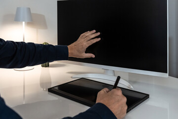 Professional interacting with a blank monitor while using a graphics tablet, poised for creative or analytical digital work