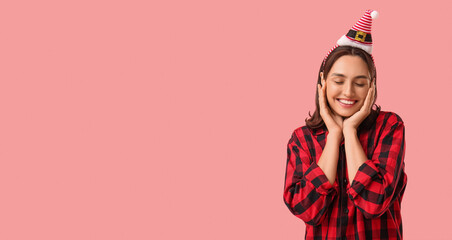 Beautiful young woman in pajamas and Santa hat on pink background
