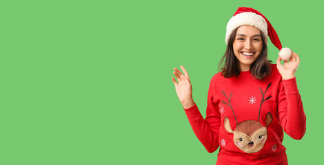 Beautiful young woman in pajamas and Santa hat on green background