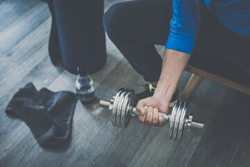 Determined sporty young man working out and trains at home. Fit male doing exercise with weights for biceps. Strong boy lifting the dumbbells in the living room. Wellness, health, sport, gym concept
