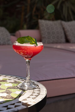 Dark red cocktail in a coup glass with basil garnish