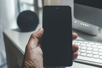 Smartphone in hand. Speaker, router, computer on desk. Technology, domotics, home automation concept