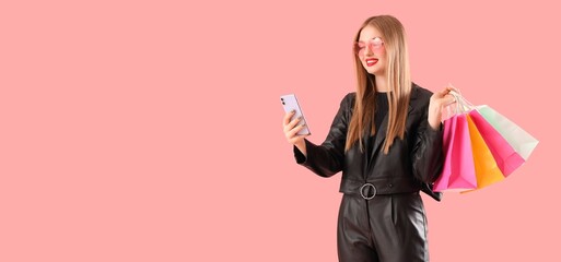 Beautiful young woman with shopping bags and mobile phone on pink background with space for text....
