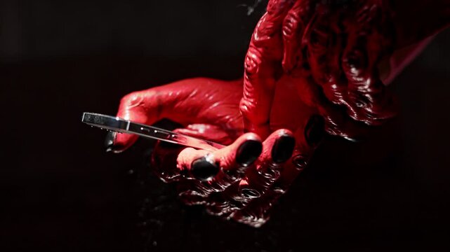 Demon, scary monster hands with claws swiping, scrolling, tapping, browsing smartphone in dark Halloween horror setting