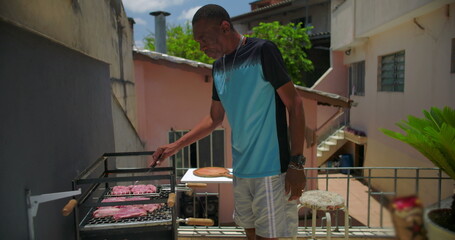 African American man grilling meat on rooftop barbecue, checking steak and sausages while preparing a meal in a vibrant outdoor urban environment