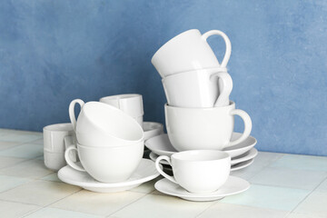 Clean cups with plates on white tile table against blue grunge wall