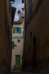 Narrow Italian alley, green shutters, rooftop antenna, satellite dish, potted plant