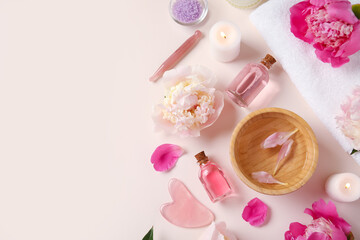 Bottles of essential oil with candles, sea salt, guasha massage tool and beautiful peony flowers on beige background