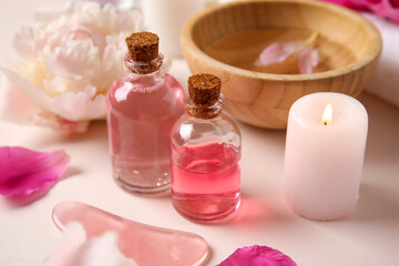 Bottles of essential oil with candle, guasha massage tool and beautiful peony flower on beige background