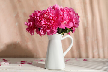 Vase with beautiful peonies on white wooden table against beige wall