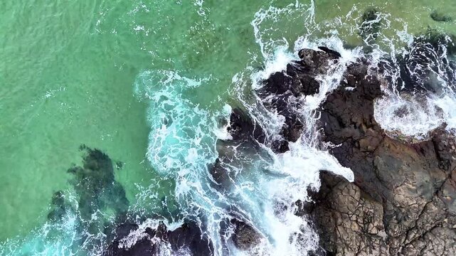 drone top aerial view ocean waves crashing against rocky island coastline 60fps 4k footage,camera pull back nature landscape ocean water foam splash on rock cliff	