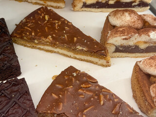 Chocolate layered cake slice with almond topping in bakery display. Concept of indulgence, craftsmanship, and sweet temptation through texture and refined dessert presentation.