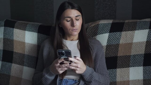 A young woman types a message on her smartphone, hesitates, and deletes it. She looks uncertain and conflicted, unsure what to say or whether to send it. Concept of hesitation, anxiety, overthinking