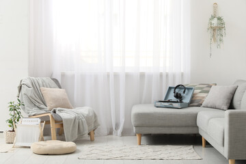 Interior of stylish living room with armchair, record player and headphones on grey sofa