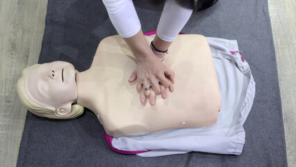CPR training on medical dummy mannequin. Person practicing chest compressions during CPR training session using a medical mannequin on a gray mat indoors.