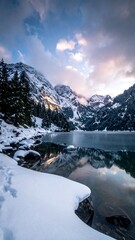 Snowy mountain landscape with a partially frozen lake reflecting the sky
