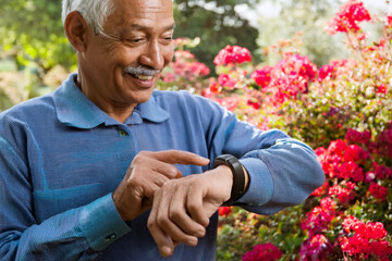 Real photo of elderly person wearing a smart health checking heart rate while gardening outside, natural daylight, plants and flowers in background