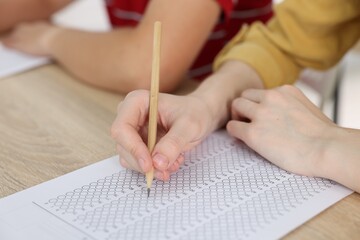 Students taking exam at wooden table indoors, closeup