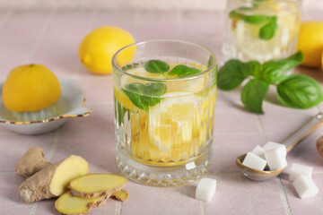 Glass of infused water with basil leaves, ginger and lemon slices on pink tile table