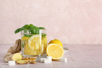 Glass of infused water with basil leaves, ginger and lemon slices on pink tile table