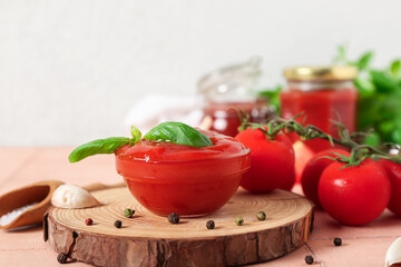 Bowl of tasty ketchup, fresh tomatoes and basil leaves on beige tile table against white wall